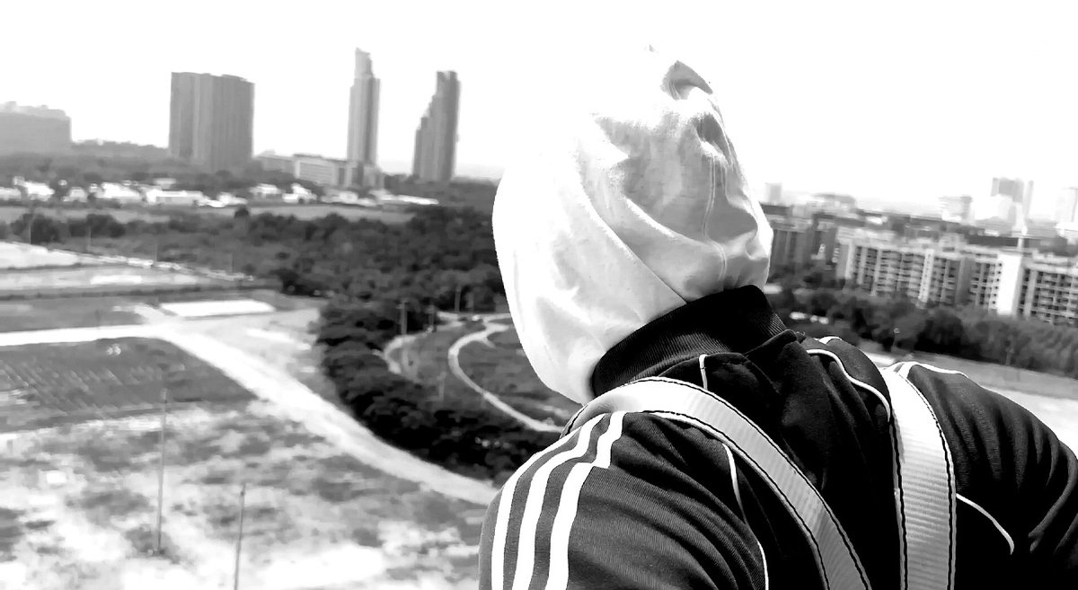 Masked figure in white hood overlooking a city landscape.